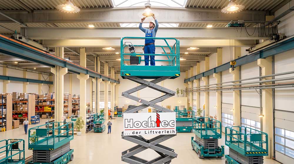 Scheren-Arbeitsbühnen von Hochtec in einer Lagerhalle, ein Monteur arbeitet an der Deckenleuchte