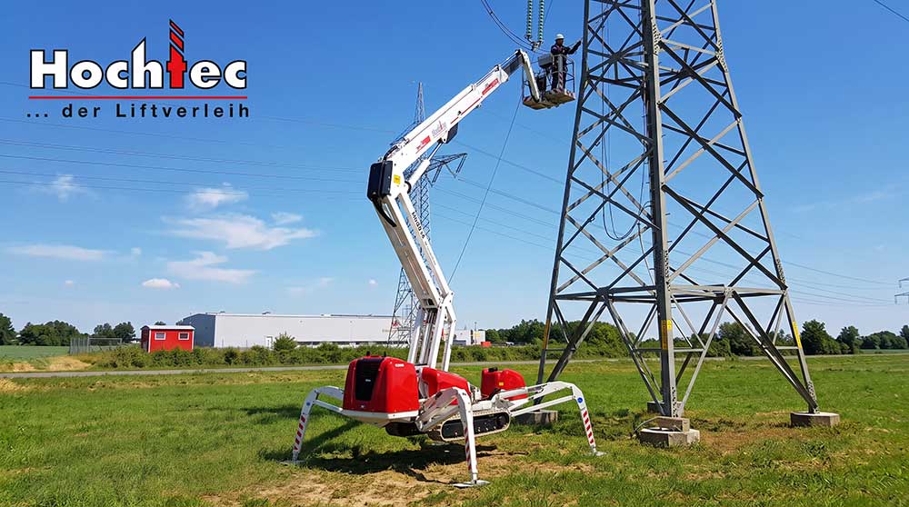 Raupen-Arbeitsbühne mit Ketten an einem Strommast auf einer Wiese