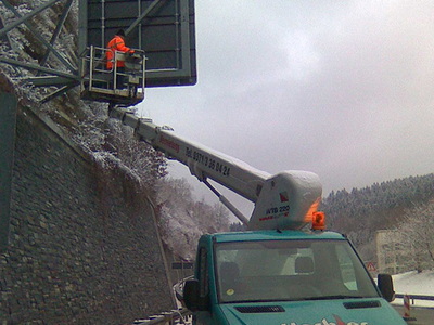 Arbeiter im Korb einer LKW-Arbeitsbühne an einer verschneiten Felswand