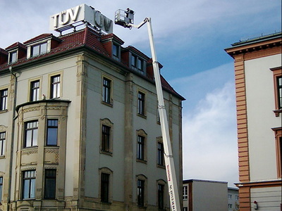 Arbeitsbühne an der TÜV-Leuchtreklame auf dem Dach eines Altbaus